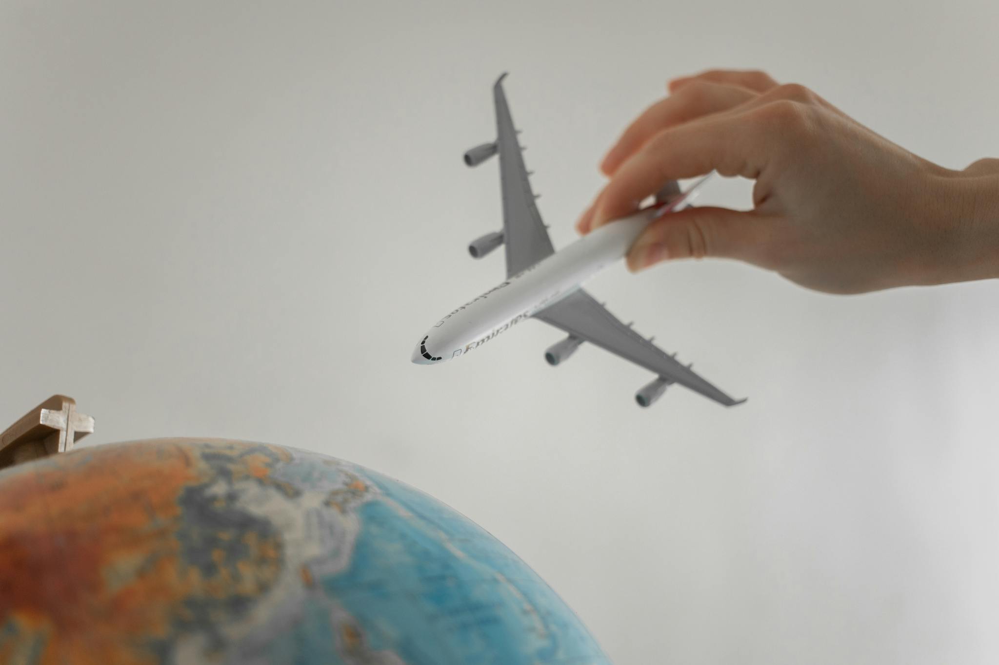 A hand holds a toy airplane above a globe, symbolizing travel and exploration.