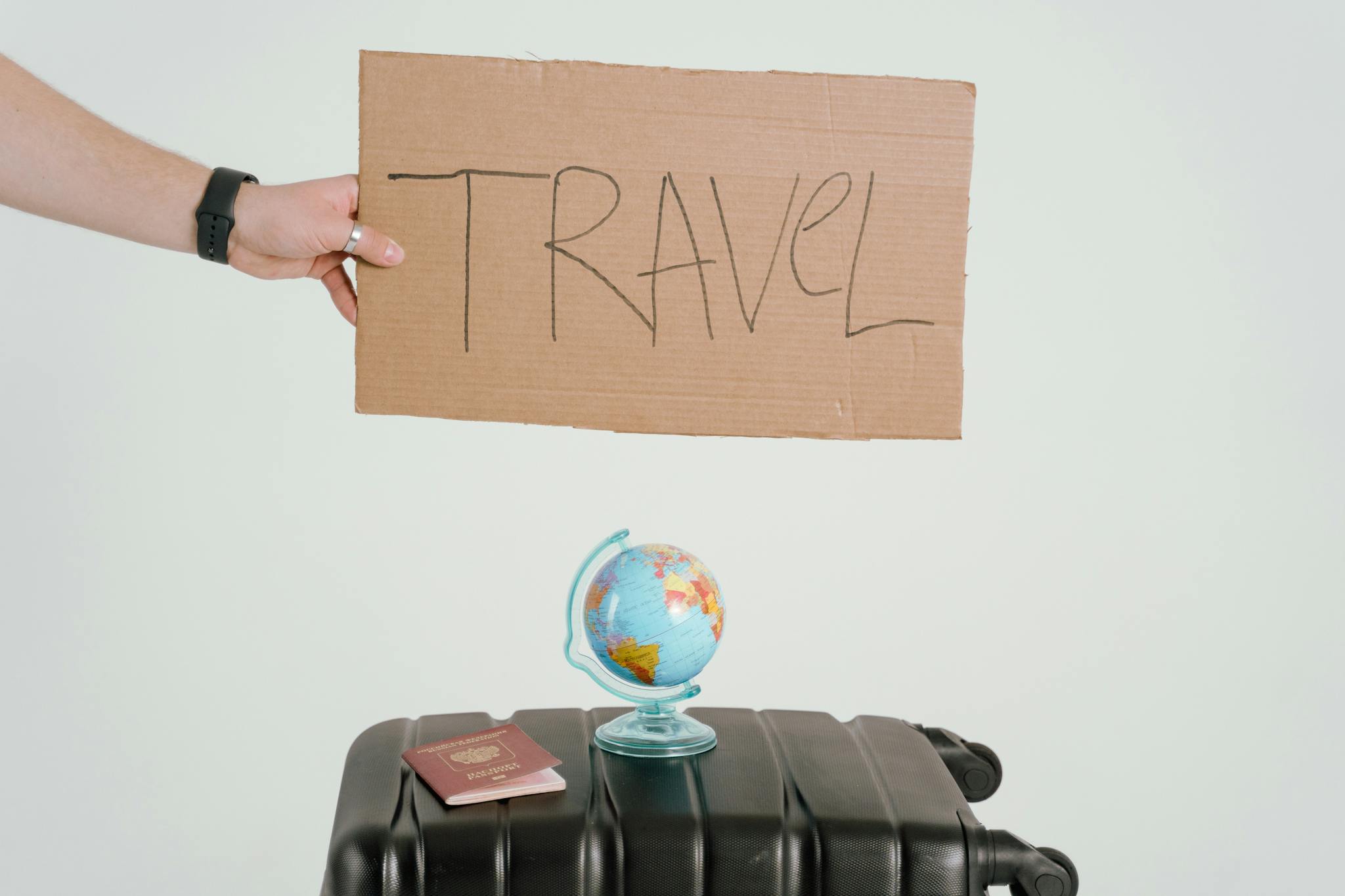 A hand holds a travel sign above a globe and suitcase, symbolizing wanderlust.